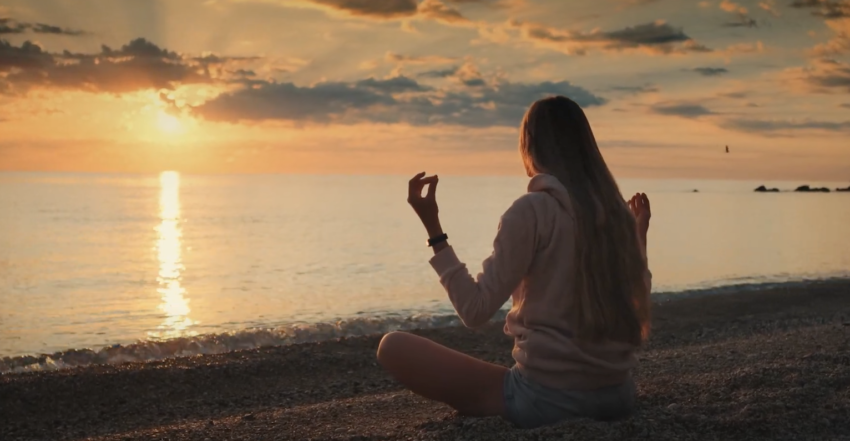 的一个女孩面对大海,坐在岸边的十字交叉,冥想太阳集
