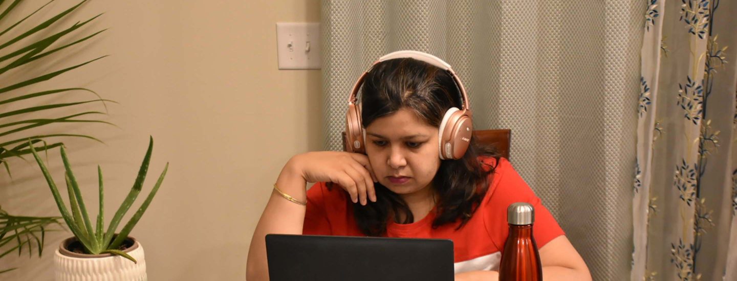一个穿着红色t恤，戴着耳机的女人在学习，身边放着笔记本电脑、水瓶和植物