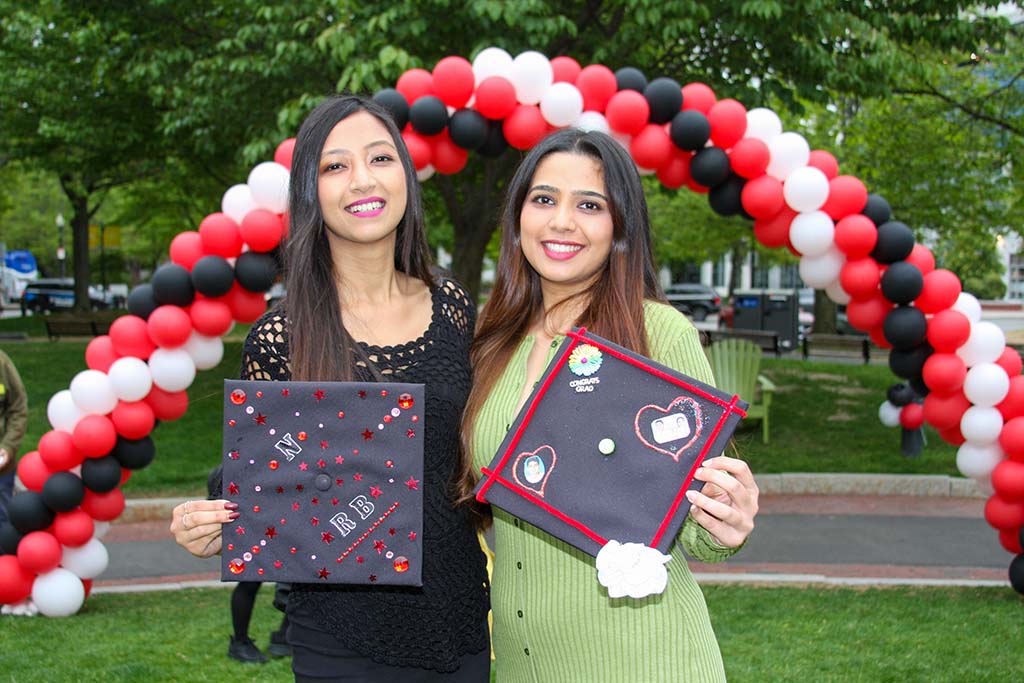 在2022年5月的毕业典礼上，两名女毕业生在女大红、白、黑三色的气球前展示她们装饰过的学士帽。丹尼斯·里德摄
