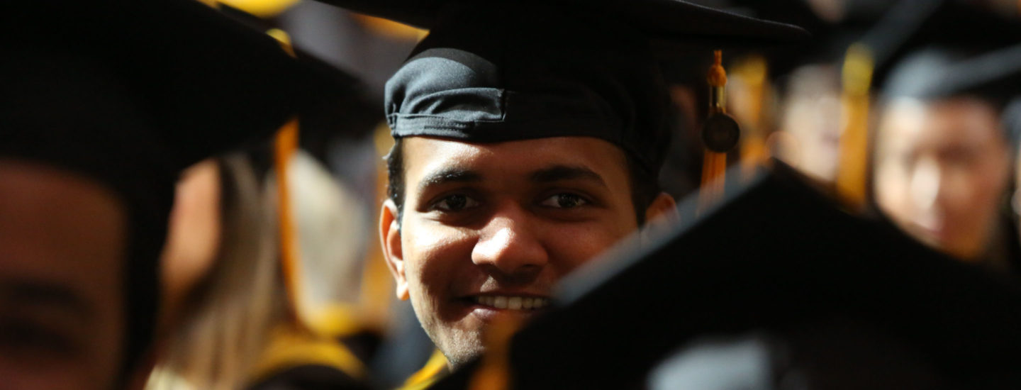 在2022年5月的CPS毕业典礼上，一名穿着学士服和学士帽的研究生在其他毕业生中微笑着看着镜头。摄影:Heratch Ekmekijan