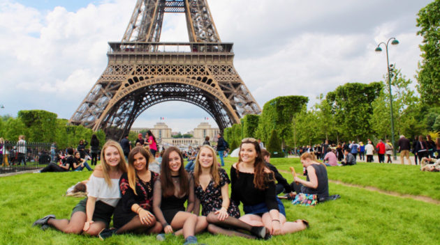 一群学生坐在埃菲尔铁塔前的草坪上。