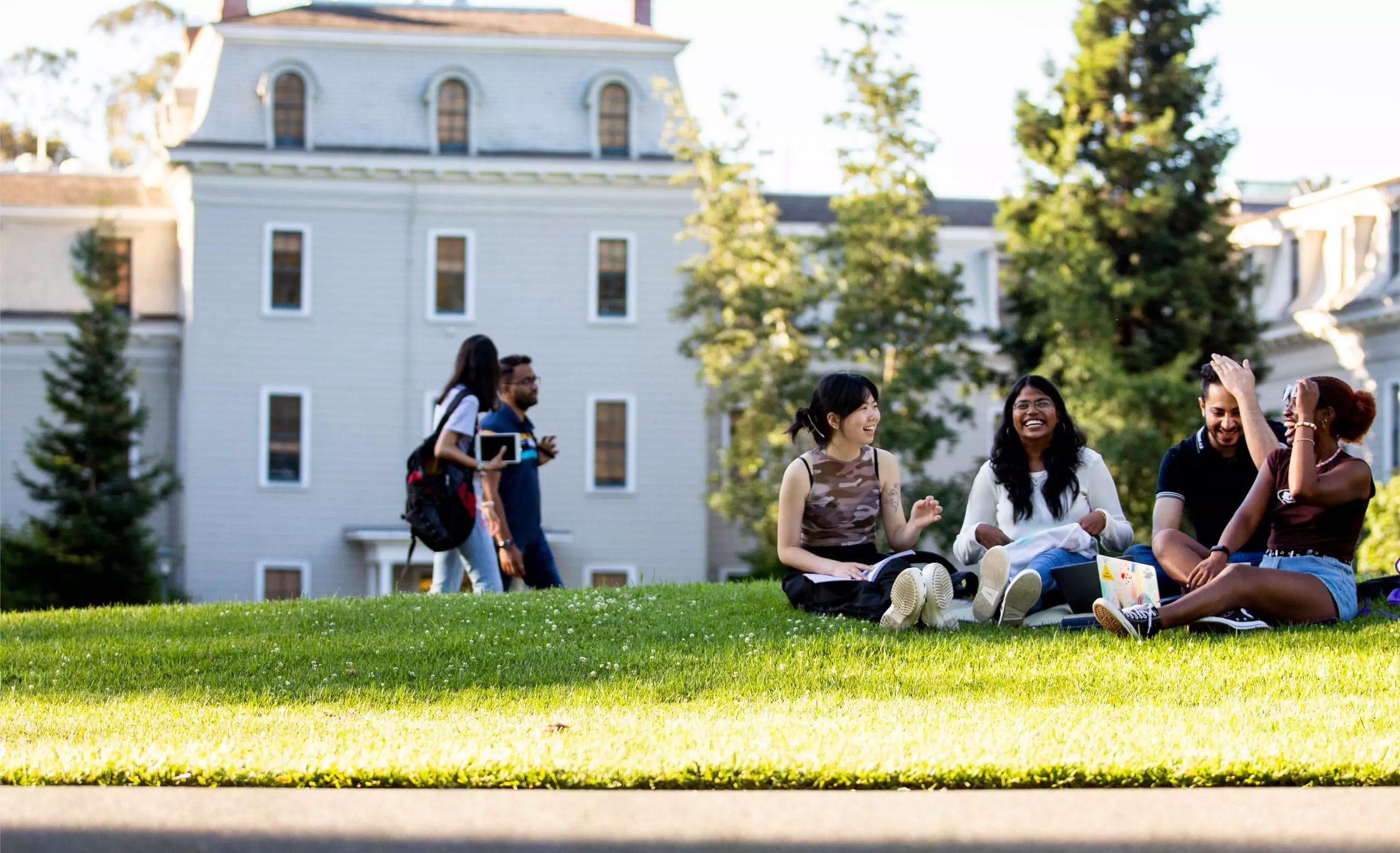 一群学生坐在Holmgren草地上，背景是东北大学奥克兰校区的米尔斯大厅。raybet雷竞技雷竞技app最新版