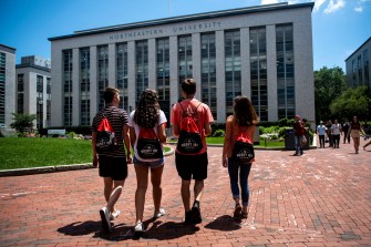 四位学生在大学大楼前手举手