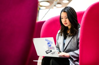 雪儿王坐粉红色椅子 ISEC工作她的笔记本电脑