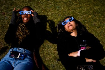 两位学生躺在草坪上看日食戴eclipse镜