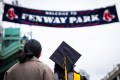 身戴帽子礼服的毕业生向上看公园外的标语“欢迎Fenway公园”。