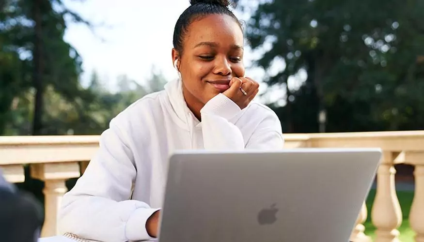 学生坐在外面对着笔记本电脑屏幕微笑