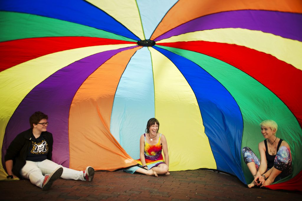 3学生坐在一个大彩虹伞